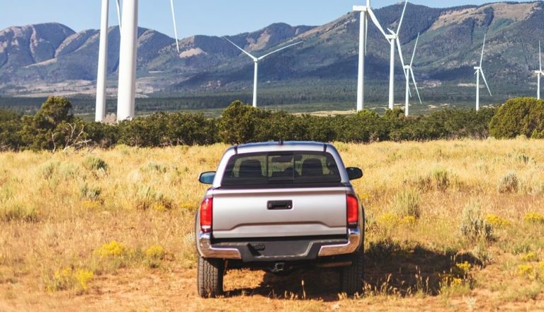 Pickup parked near a wind farm, with mountains in the background.