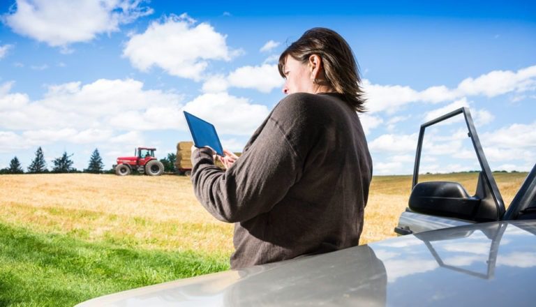 Woman on a farm using a digital tablet with a tractor in the background.