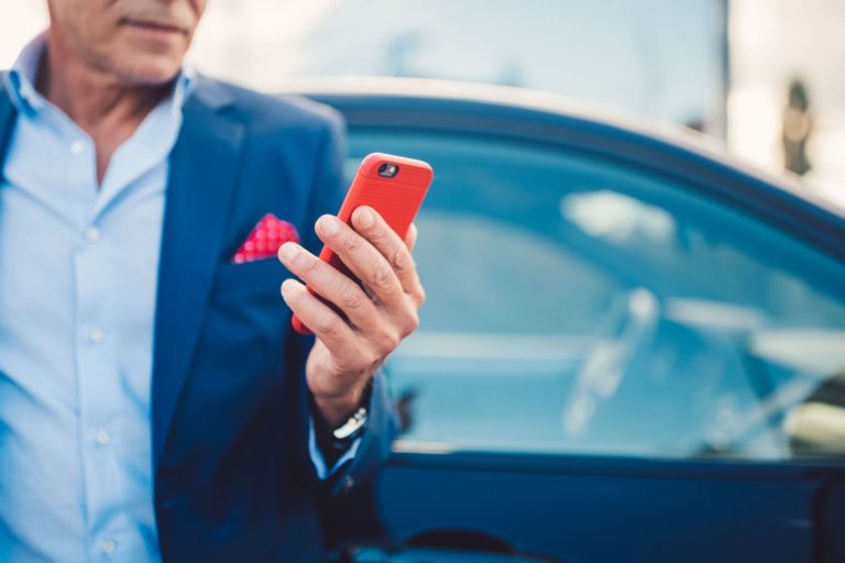 Man in blue suit holding up cellphone outside of the passenger side of a sedan