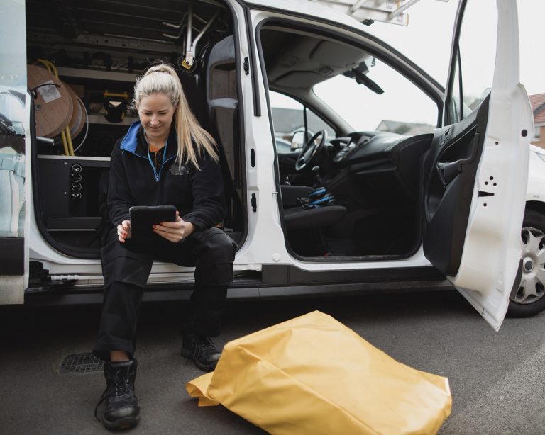 Female worker sitting in her work van while on a job and using a digital tablet.